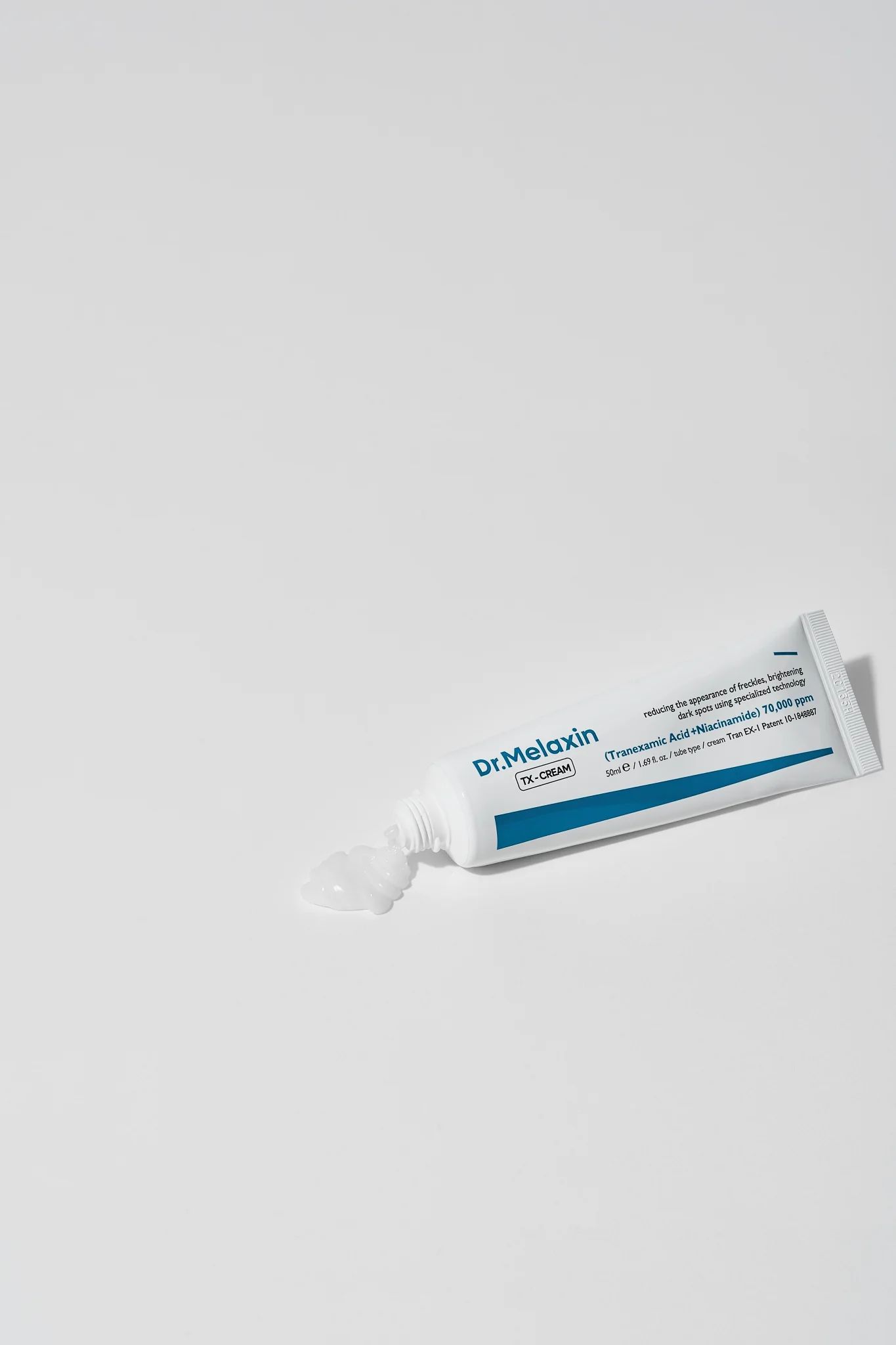 Weiße Tube mit blauer Beschriftung, Creme tritt aus. Aufschrift: Dr.Melaxin TX-CREAM. Enthält Tranexamsäure und Niacinamid.