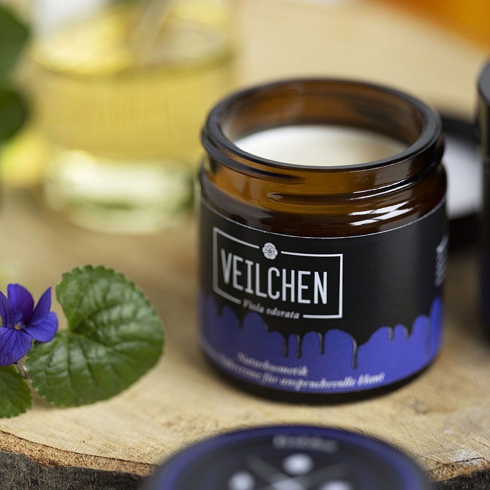 Braunes Glas mit weißer Creme. Aufschrift VEILCHEN, darunter Viola odorata. Blaue Farbstreifen. Naturkosmetik, intensive Nährcreme für anspruchsvolle Haut.
