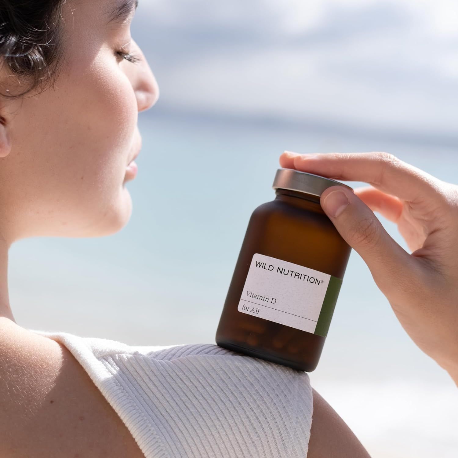 Bernsteinfarbene Glasflasche mit Wild Nutrition Vitamin D Etikett, die auf der Schulter einer Frau ruht.