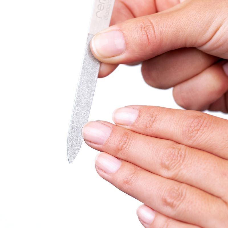 Nahaufnahme einer Nagelfeile in Anwendung. Silberfarbenes Metall, abgerundete Spitze. Hände feilen einen Nagel.