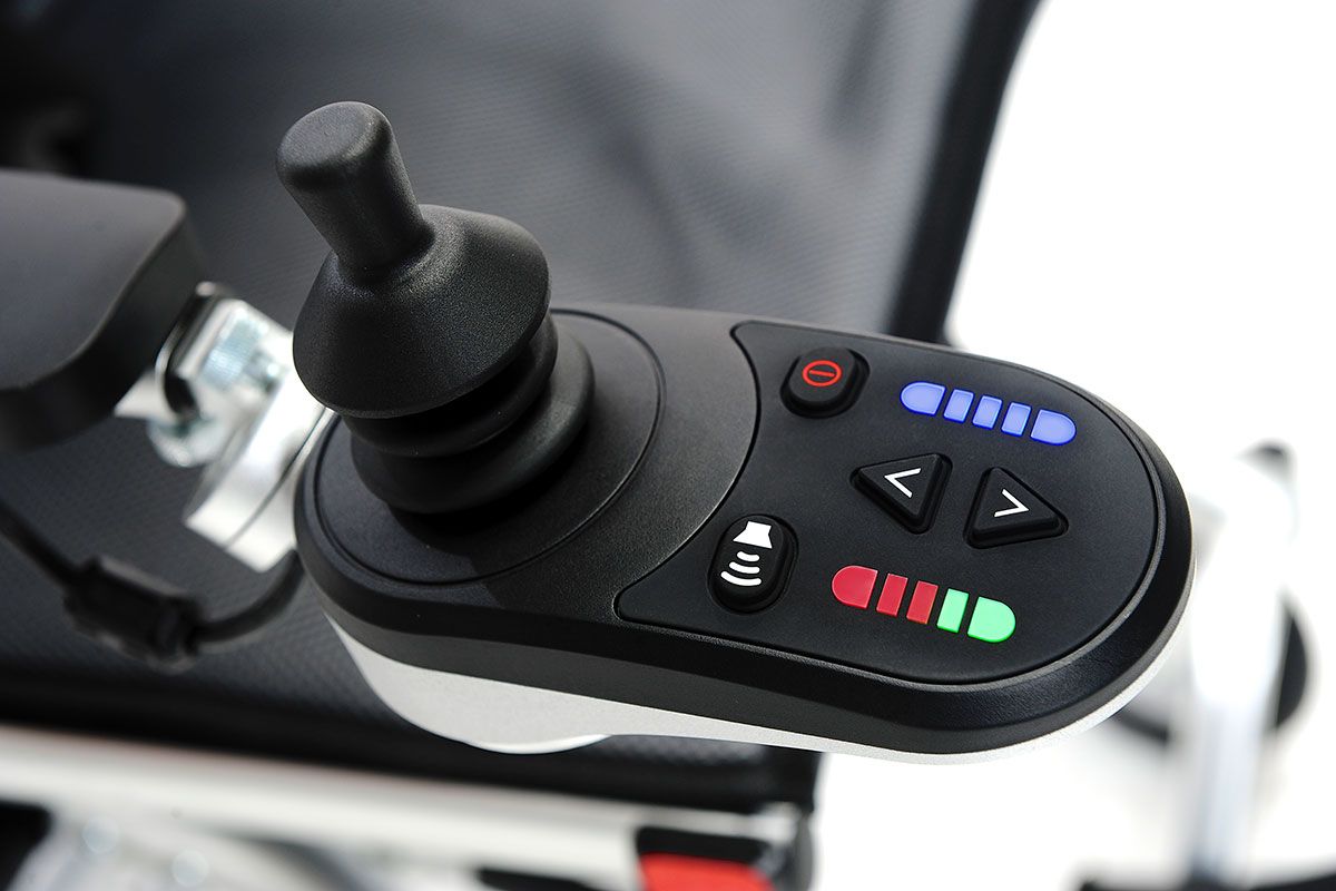 Nahaufnahme des Joysticks eines Elektrorollstuhls. Schwarzer Joystick, farbige LEDs, Bedienknöpfe.