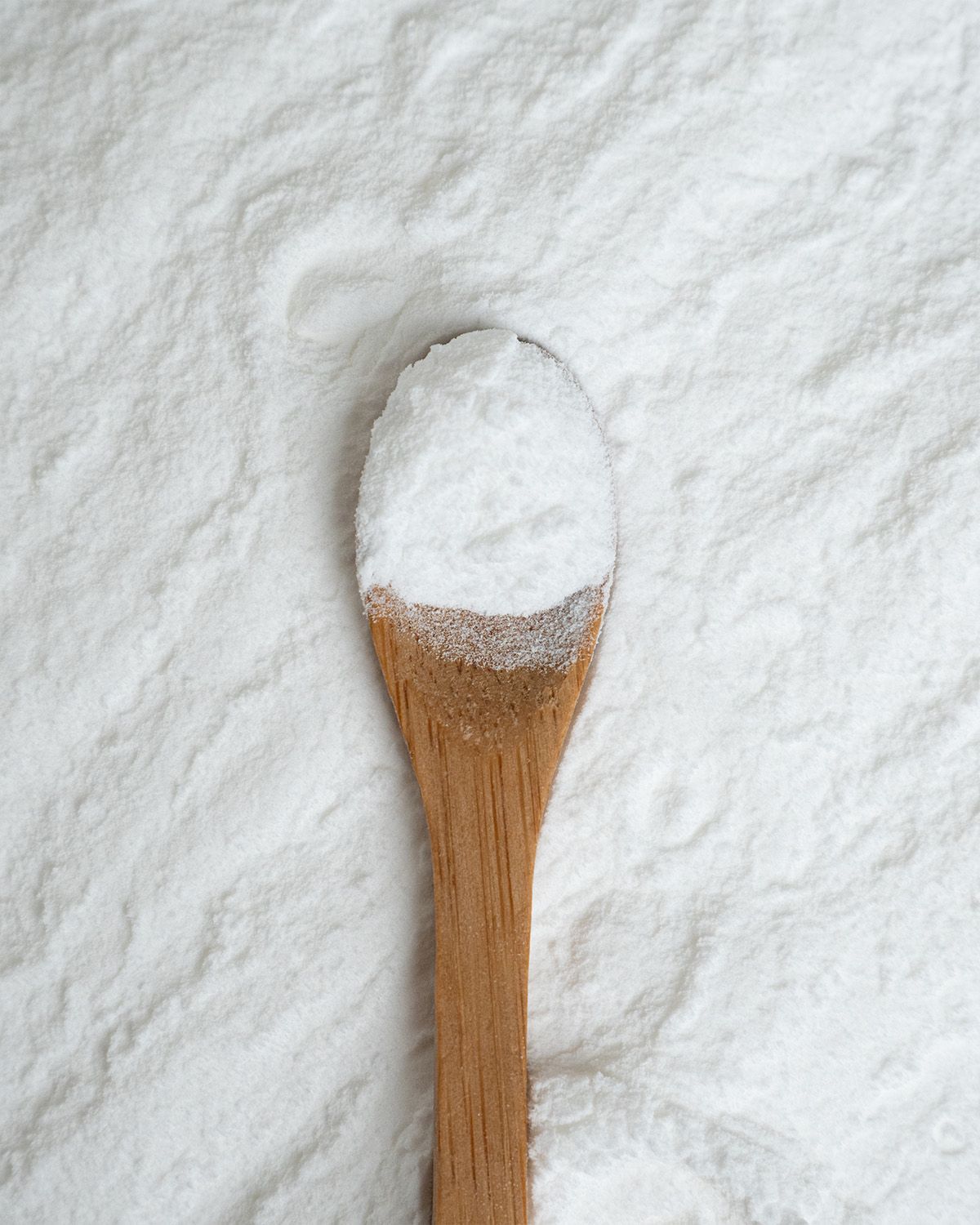 Ein Holzlöffel gefüllt mit weißem Pulver, auf einer Oberfläche aus Pulver.