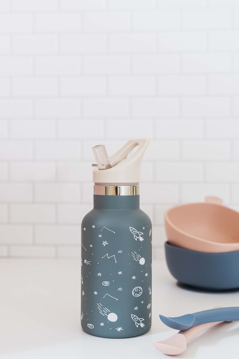 Blaue Edelstahl-Trinkflasche mit Weltraum-Motiv. Mit Trinkaufsatz. Neben Schalen und Löffeln.