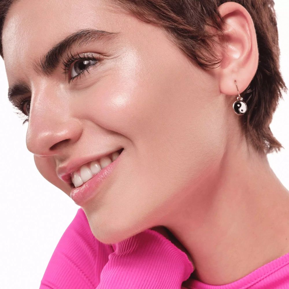 Porträt einer Frau mit Yin-Yang-Ohrringen. Sie lächelt. Hautton: hell.