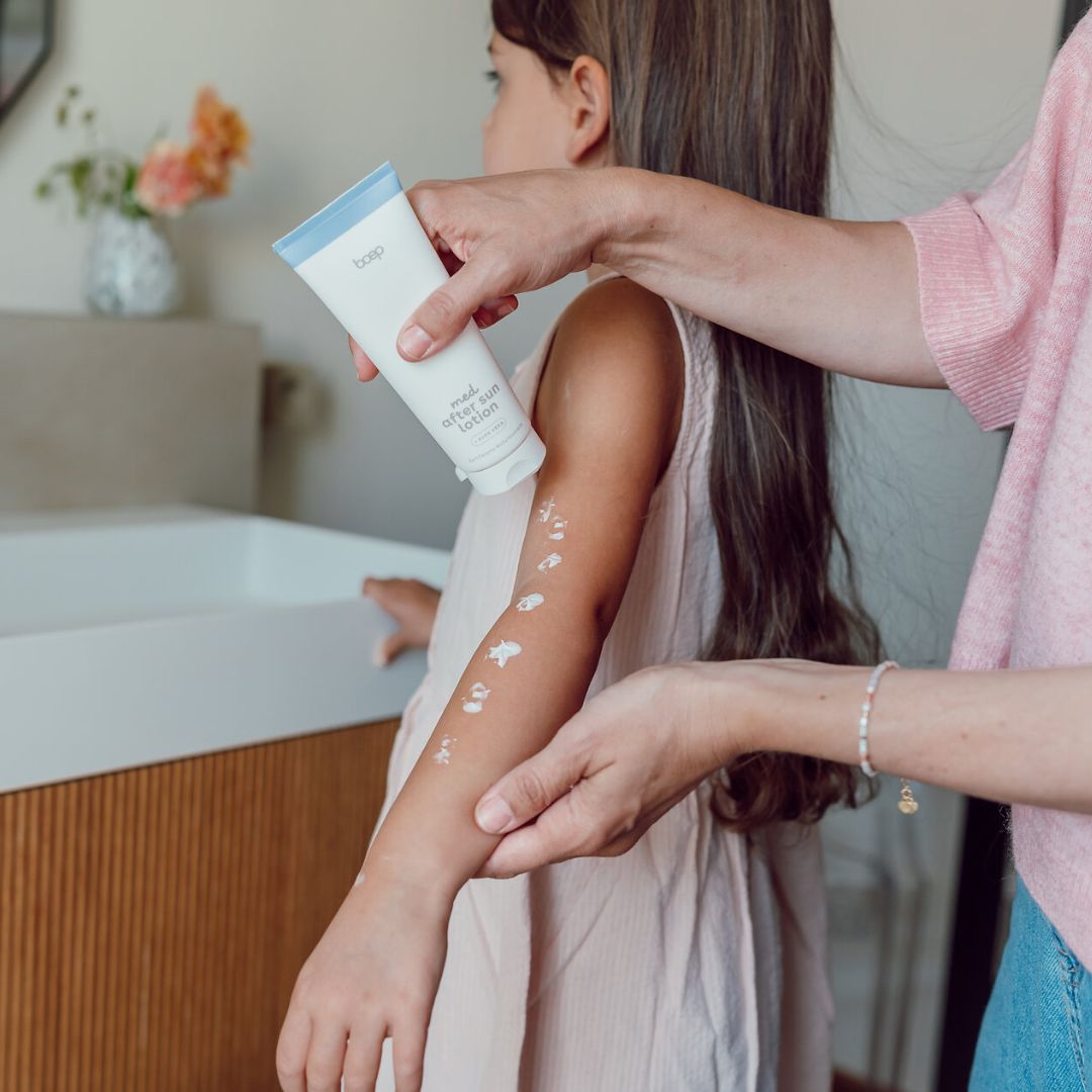 Person trägt med after sun lotion auf Arm eines Kindes auf. Produkt in weißer Tube.