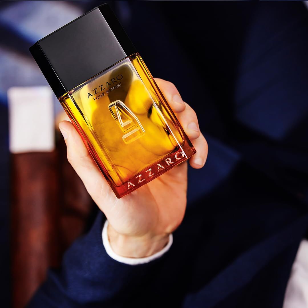 Azzaro Pour Homme Flakon in einer Hand. Rechteckiger Flakon mit schwarzem Deckel. Gelbe Flüssigkeit. Person trägt Blazer.