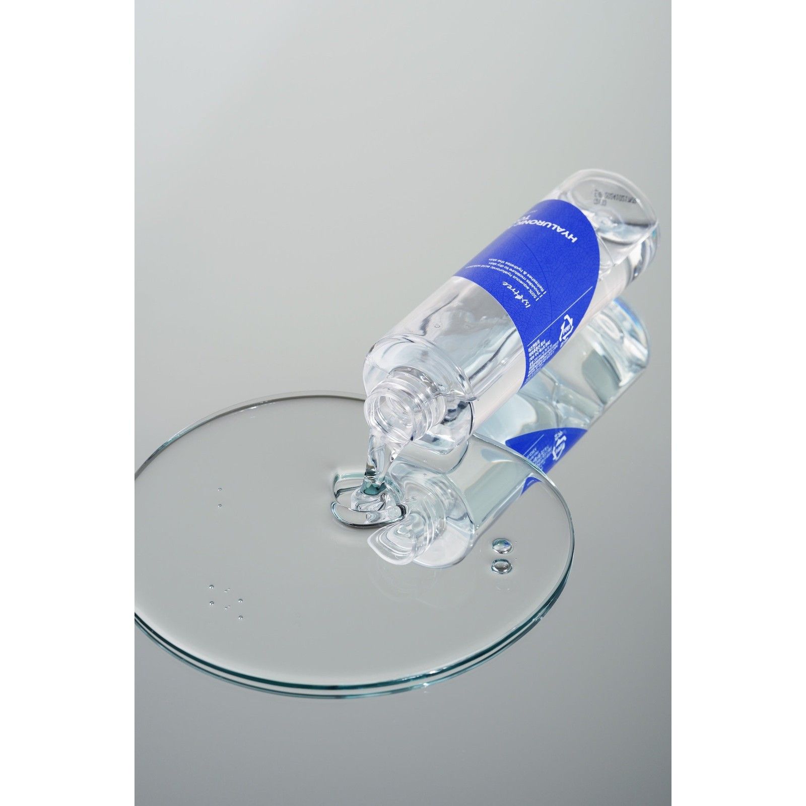 Isntree Hyaluronic Acid Toner fließt aus einer Flasche auf eine spiegelnde Oberfläche und bildet einen großen Tropfen.