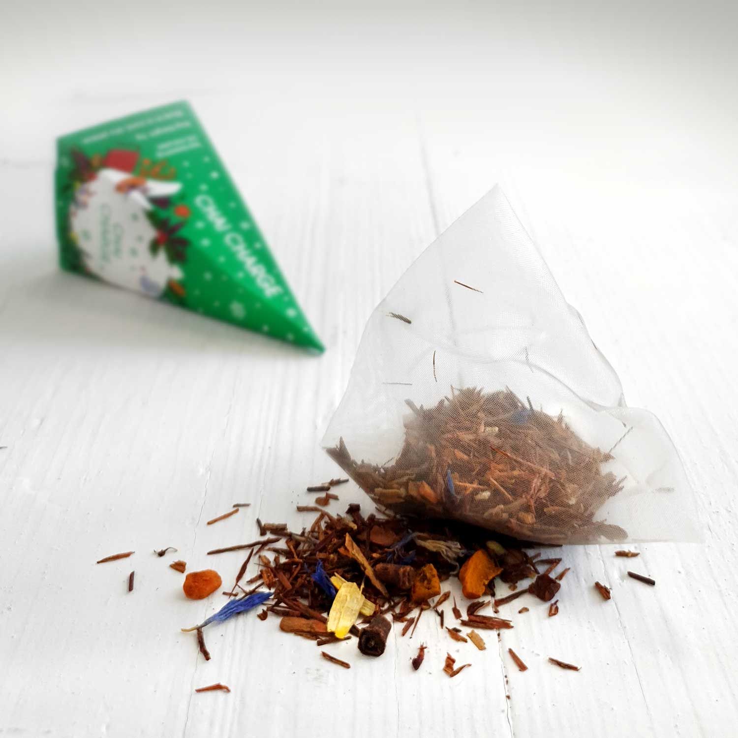 Offener Teebeutel mit losem Tee. Daneben ein grüner pyramidenförmiger Teebeutel. Aufdruck: English Tea Shop.