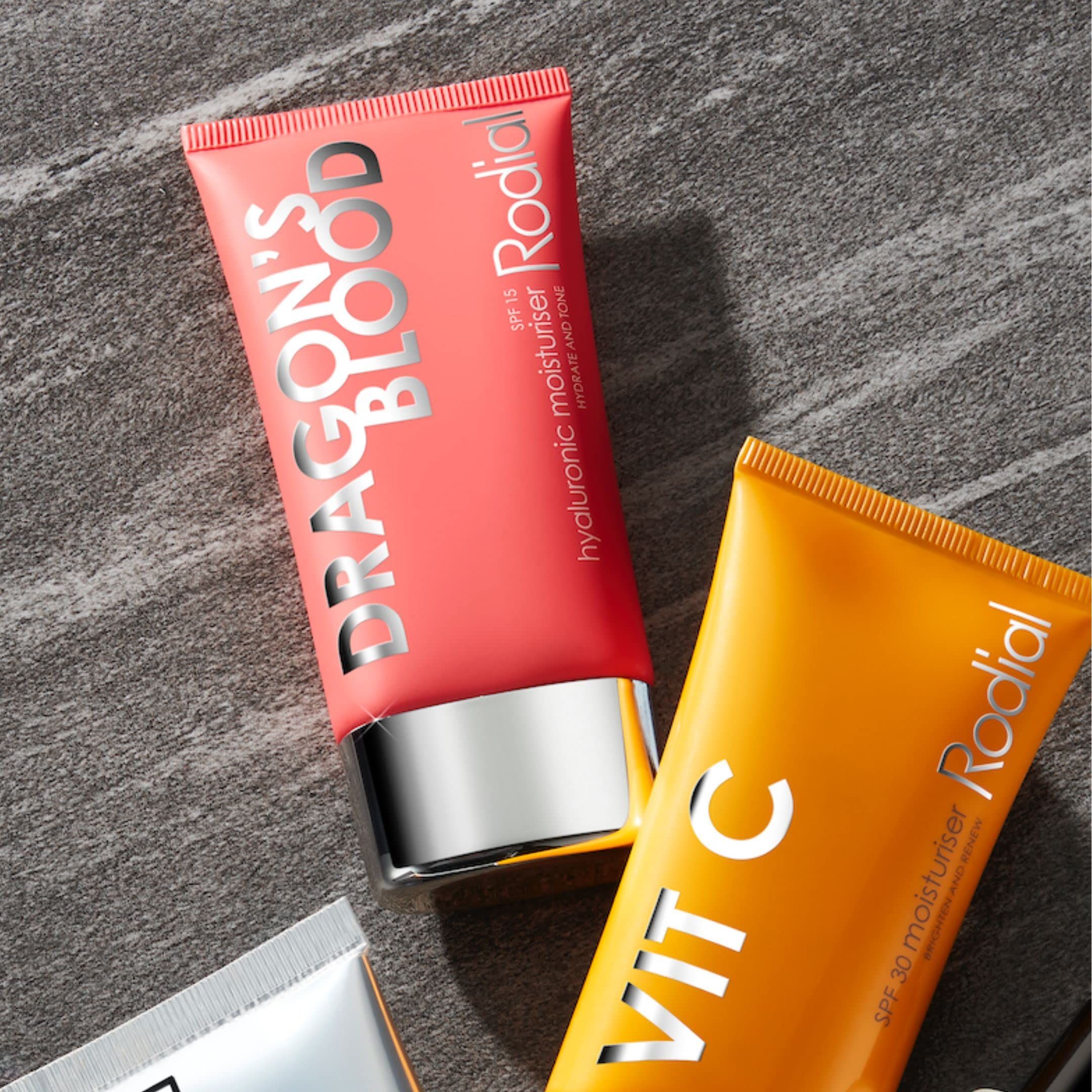 Zwei Tuben. Rote Tube mit weißer Schrift: DRAGON'S BLOOD, Rodial. Gelbe Tube: VIT C. Produktname: Hyaluronic Moisturiser. Auf grauem Untergrund.
