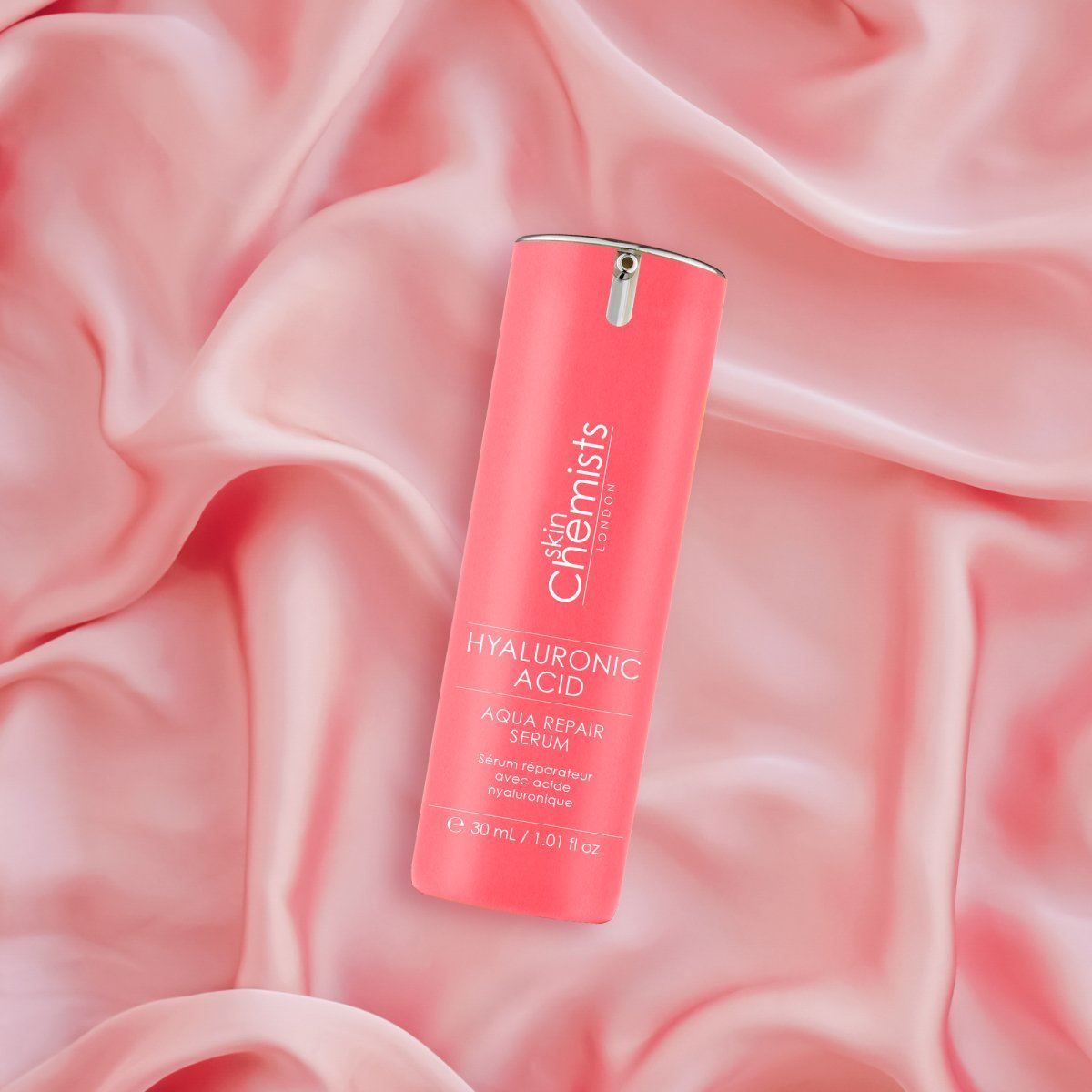 SkinChemists Hyaluronsäure Aqua Repair Serum Flasche auf rosa Seide.