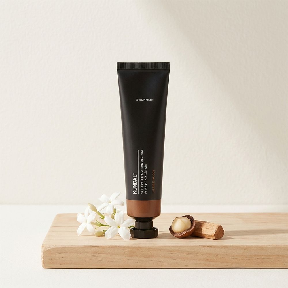 Schwarze Tube Handcreme mit braunem Boden. Aufschrift: KUNDAL Shea Butter & Macadamia Pure Hand Cream. Daneben Holz, Blüten und Nüsse.