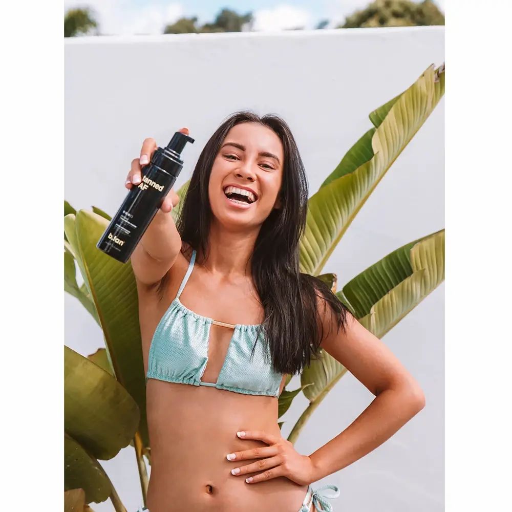 Schwarze Sprühflasche mit 'Tanned AF' und 'B.Tan' Aufschrift, gehalten von einer Frau.
