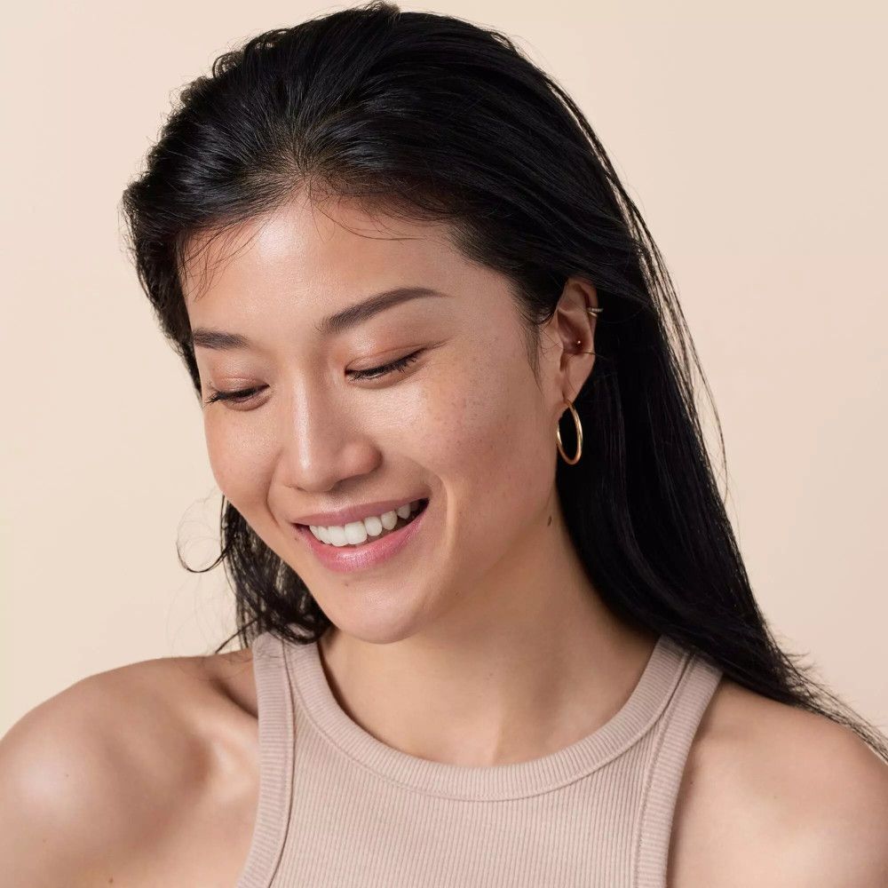Eine lächelnde Frau mit dunklen Haaren und einem Tanktop. Sie hat goldene Ohrringe.