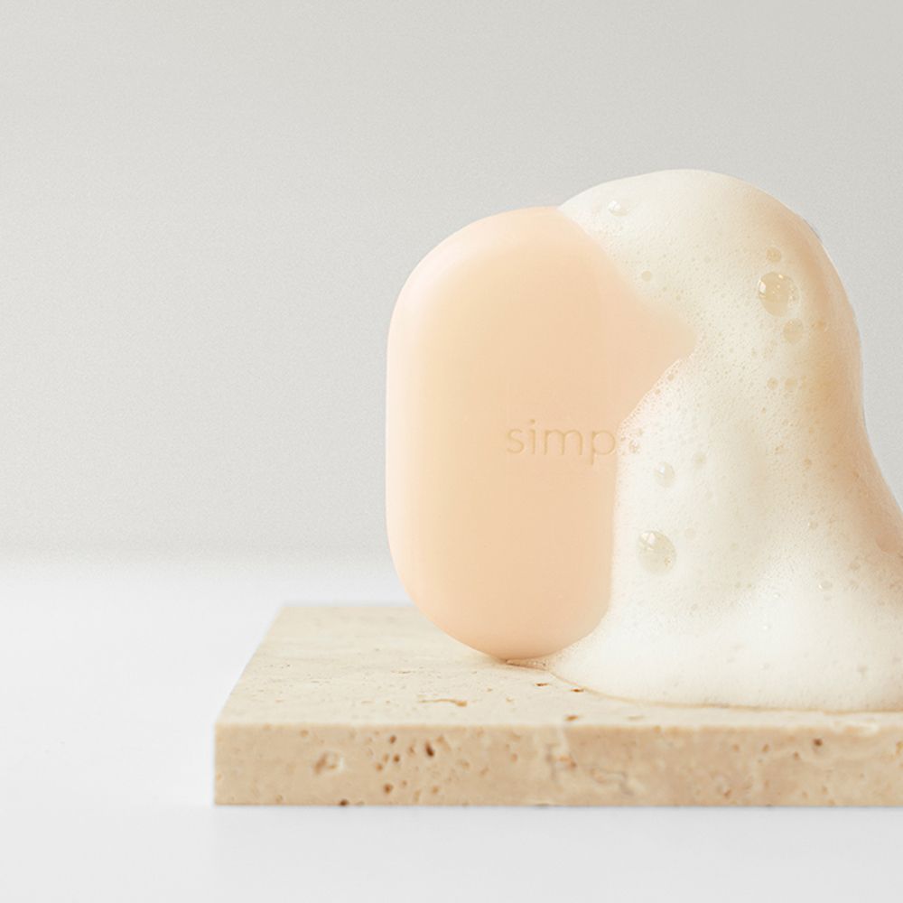 Beige Shampoo-Bar auf Steinplatte mit Schaum. Logo sichtbar. Produkt in Anwendung.