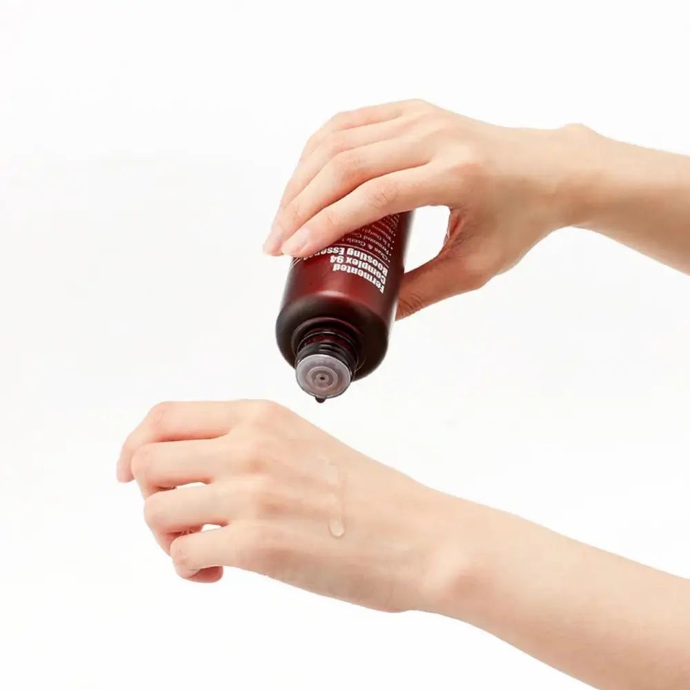 Hände halten eine braune Flasche. Flüssigkeit tropft auf eine Hand. Produktname nicht sichtbar.