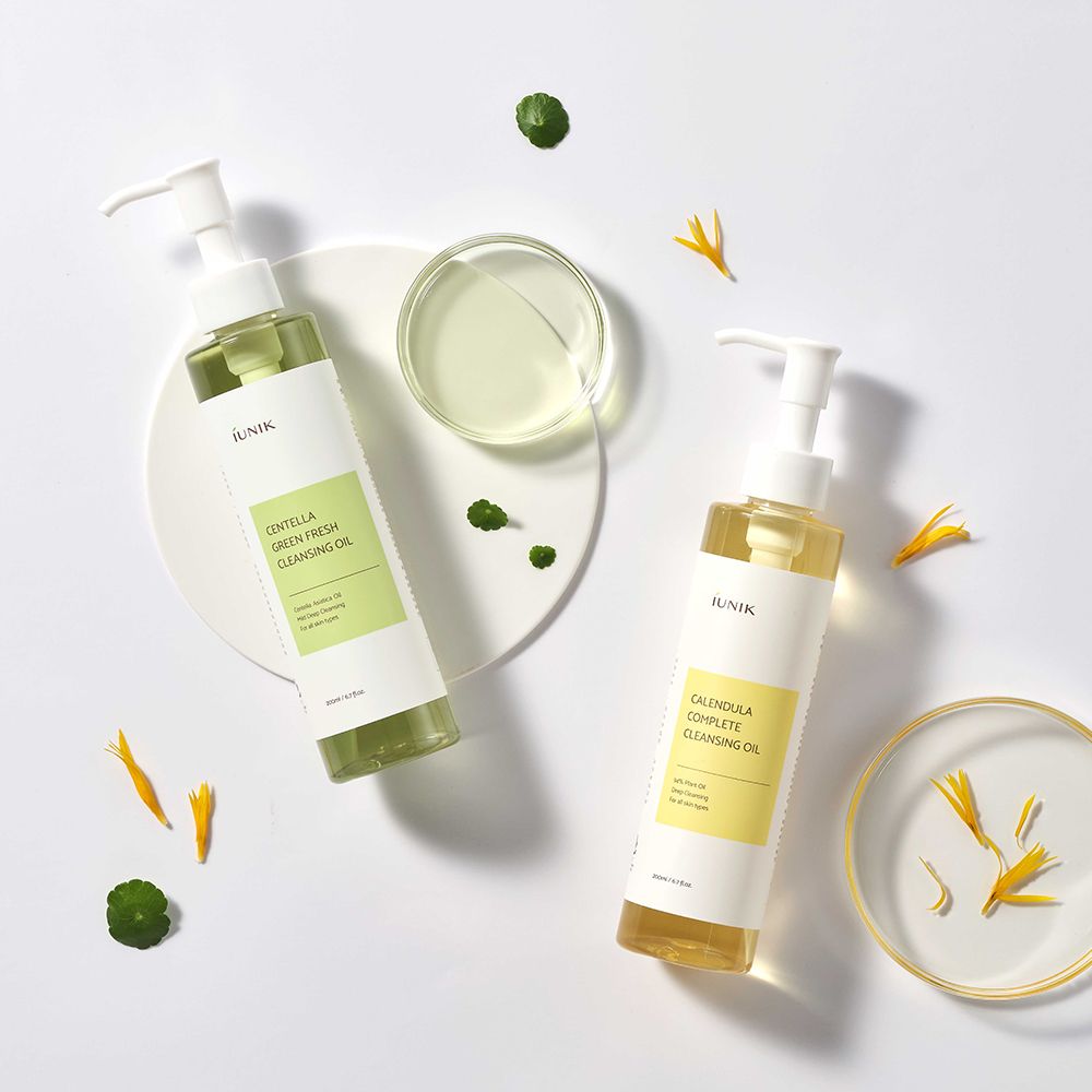 Zwei iUNIK Cleansing Oils, eines grün, eines gelb, mit Blütenblättern.