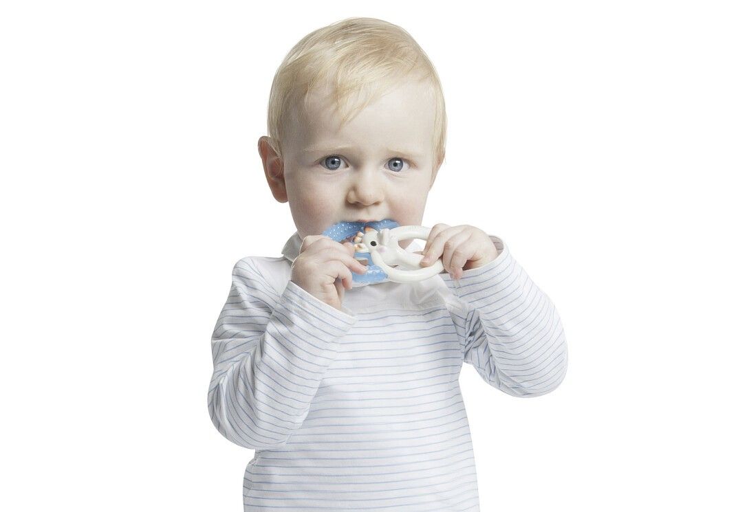 Kleinkind beißt auf Beißring. Giraffen-Design, blauer Ring. Kind trägt gestreiftes Shirt.