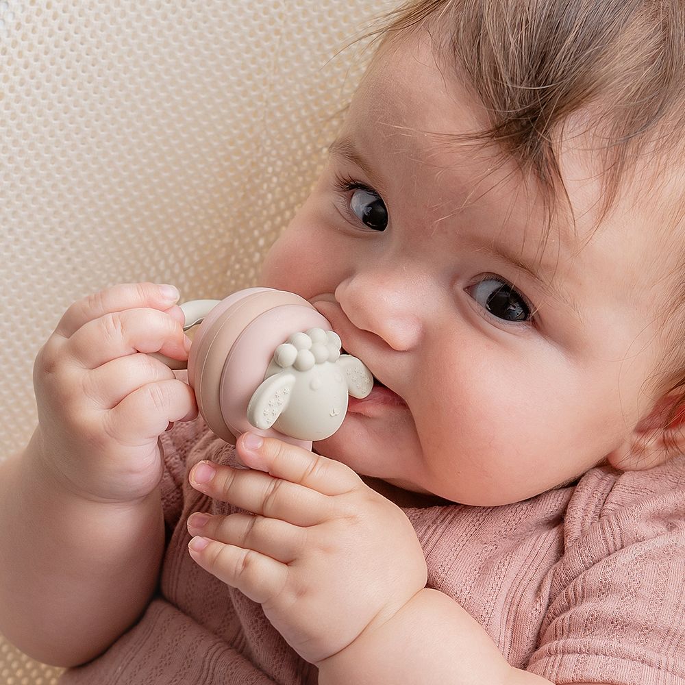 Ein Baby kaut auf einem bunten Beißring in Schaf-Form.