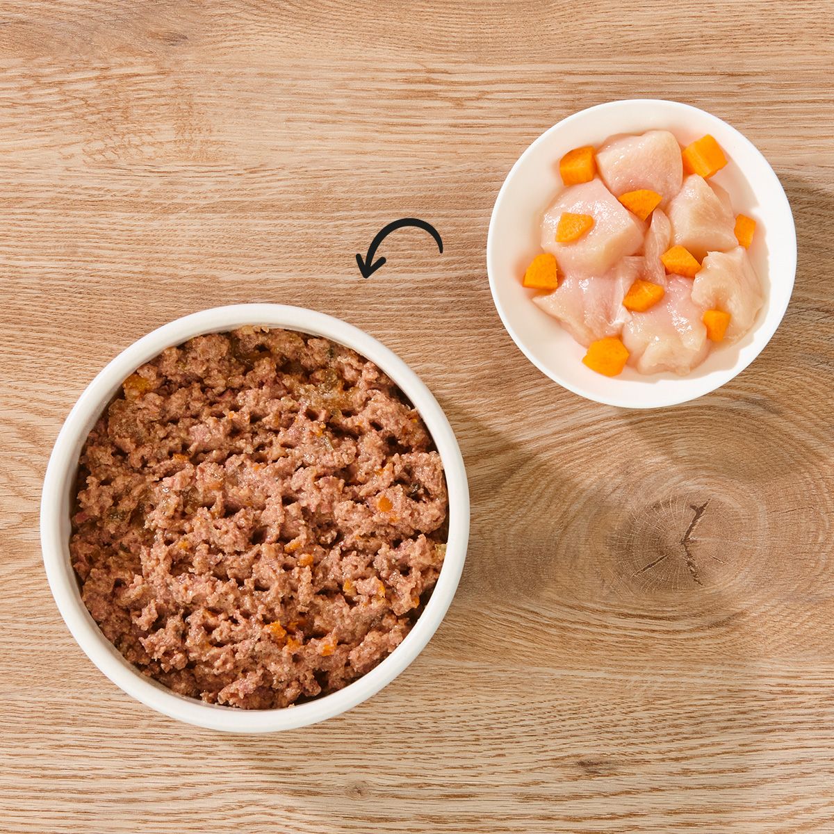 Zwei Schalen mit Hundefutter. Links: Futterbrei. Rechts: Hühnerfleisch und Karottenstücke. Pfeil zeigt von rechts nach links.
