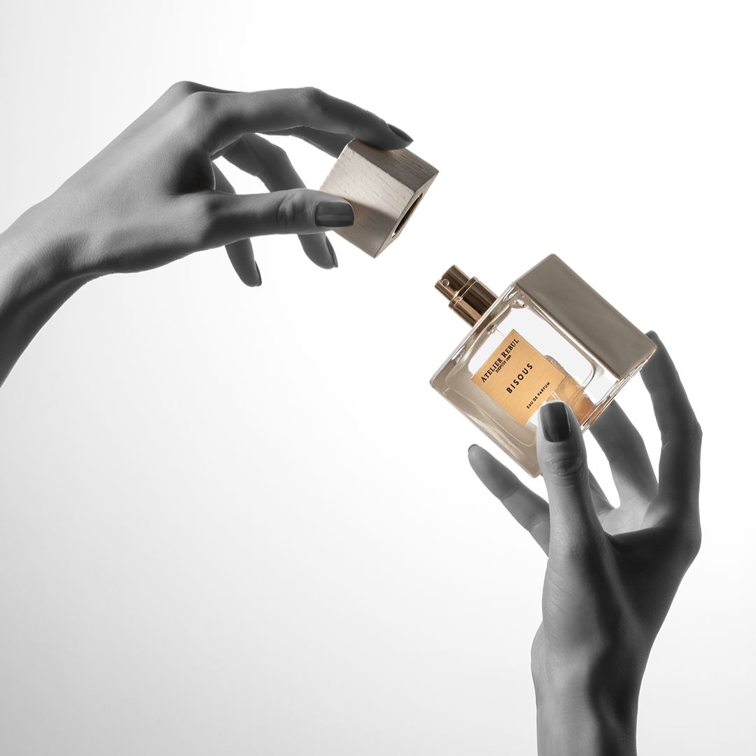 Hände halten eine quadratische Glasflasche und einen Holzdeckel. Auf der Flasche steht "Bisous".