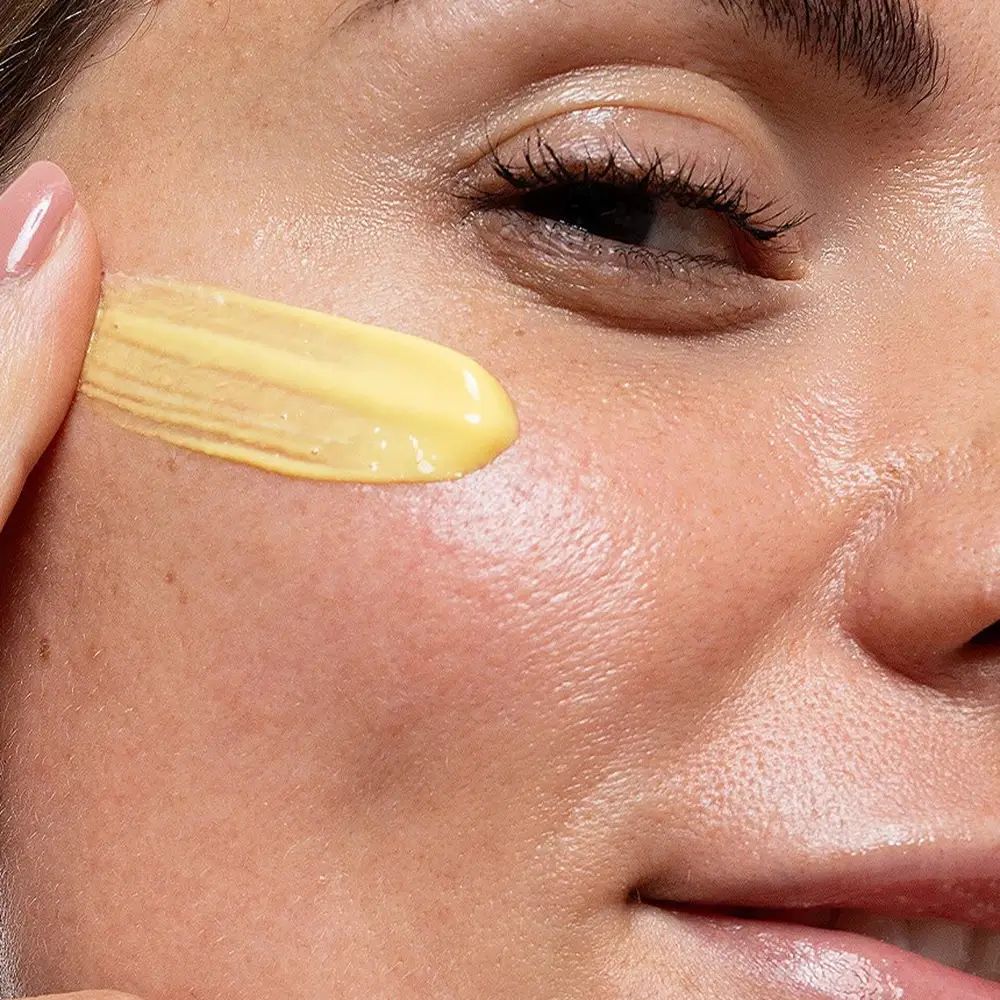 Nahaufnahme einer Frau, die Creme auf ihre Wange aufträgt. Gelbe Creme wird aufgetragen.