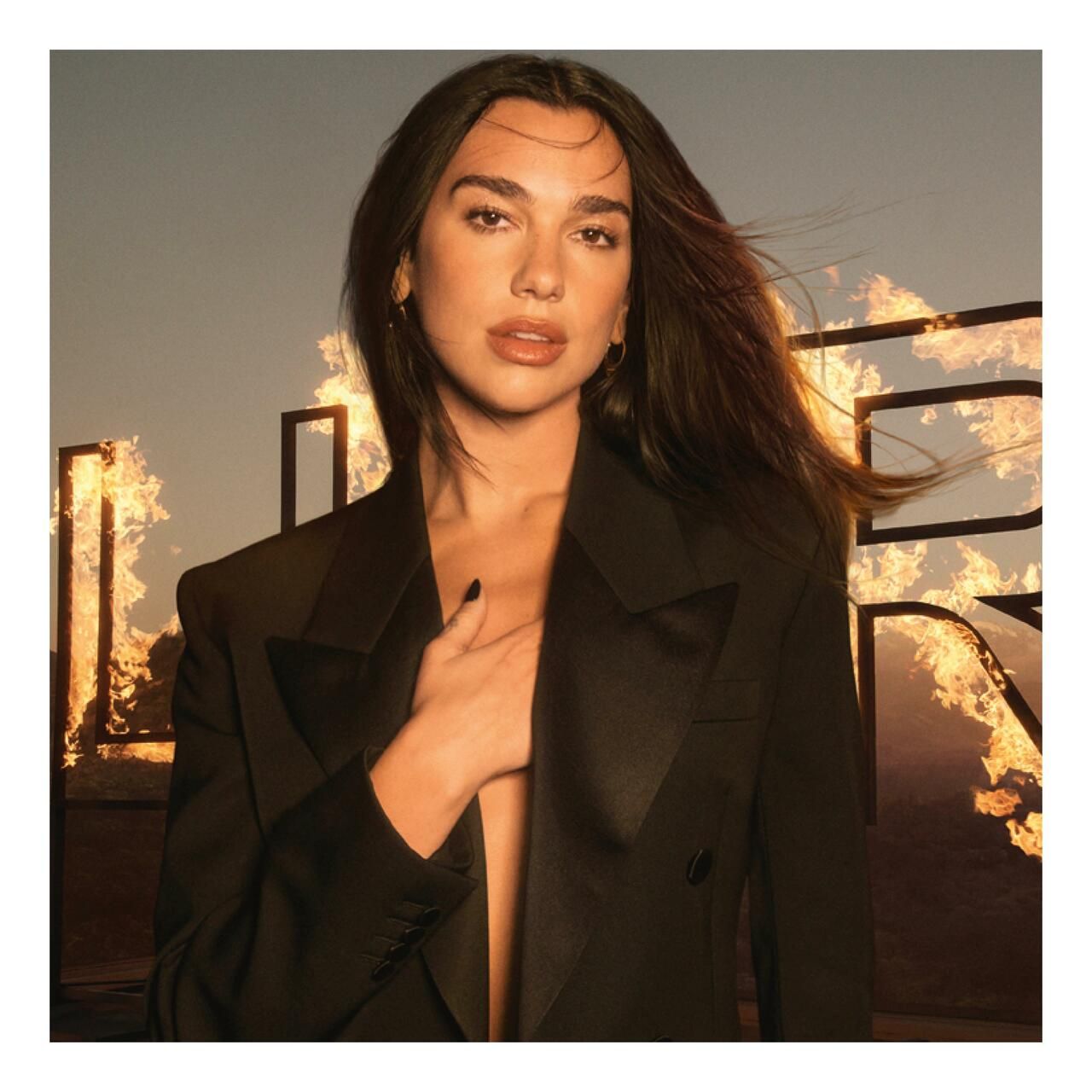 Dua Lipa vor einem Hintergrund mit Flammen und dem Wort LIBRE. Sie trägt einen schwarzen Blazer.