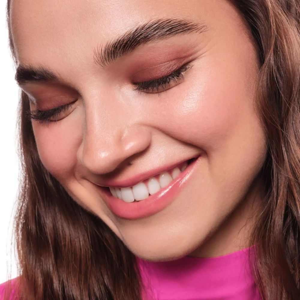 Porträt einer lächelnden Frau mit geschlossenen Augen. Sie trägt rosa Make-up.