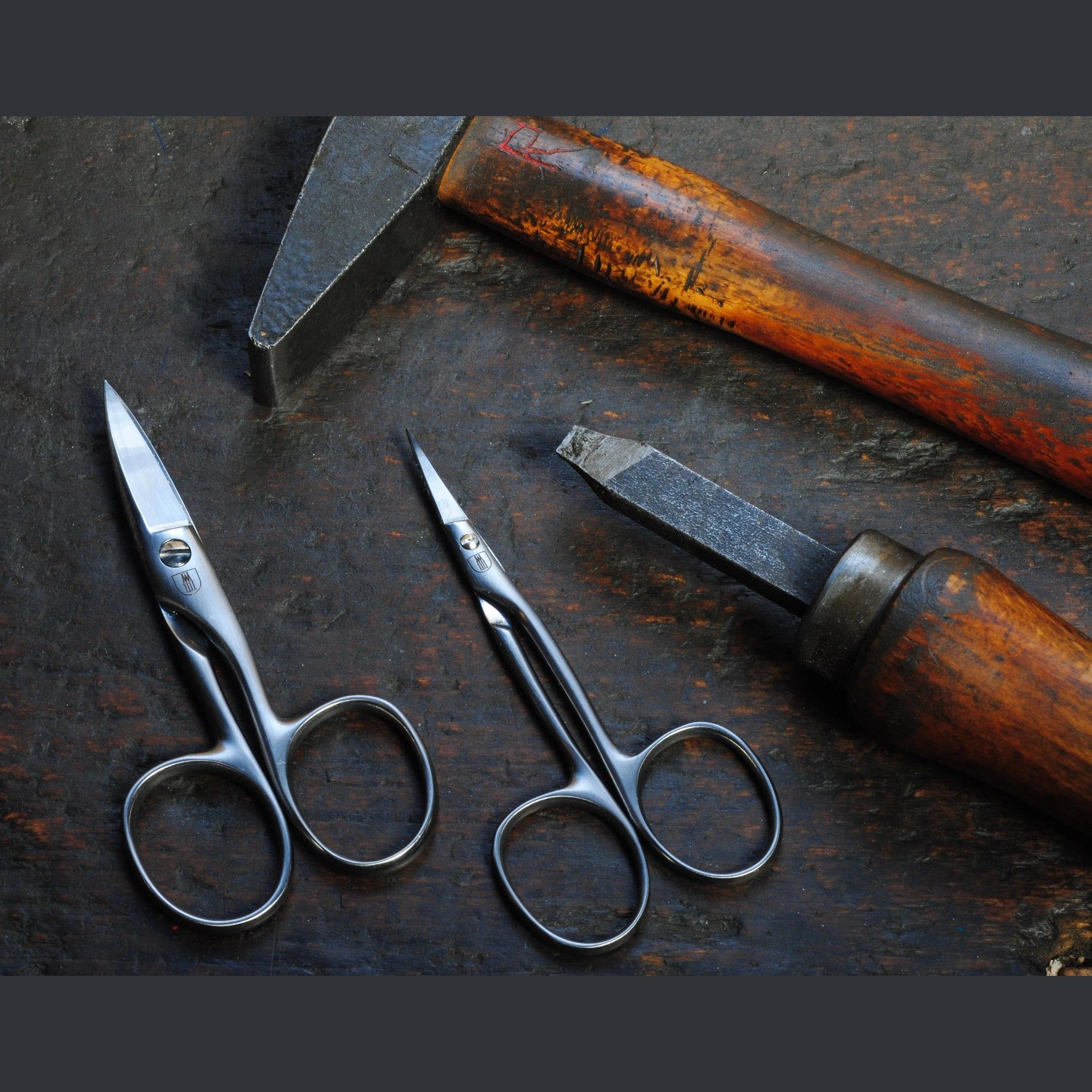 Zwei Nagelhautschere neben Hammer und Meißel. Metall, gebogene Klingen, runde Griffe.