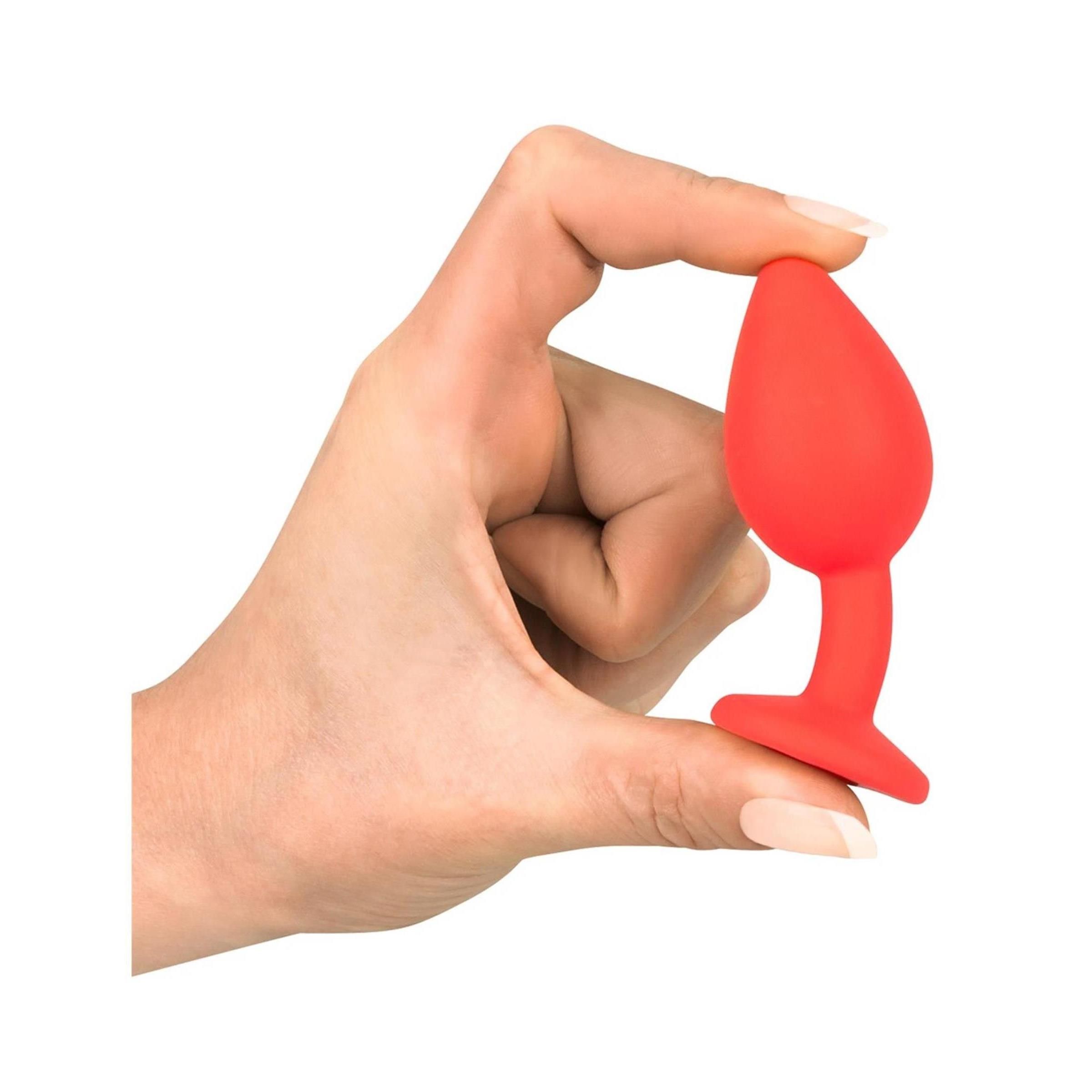 Roter Plug in einer Hand gehalten. Kegelförmiger Aufsatz, runder Sockel.