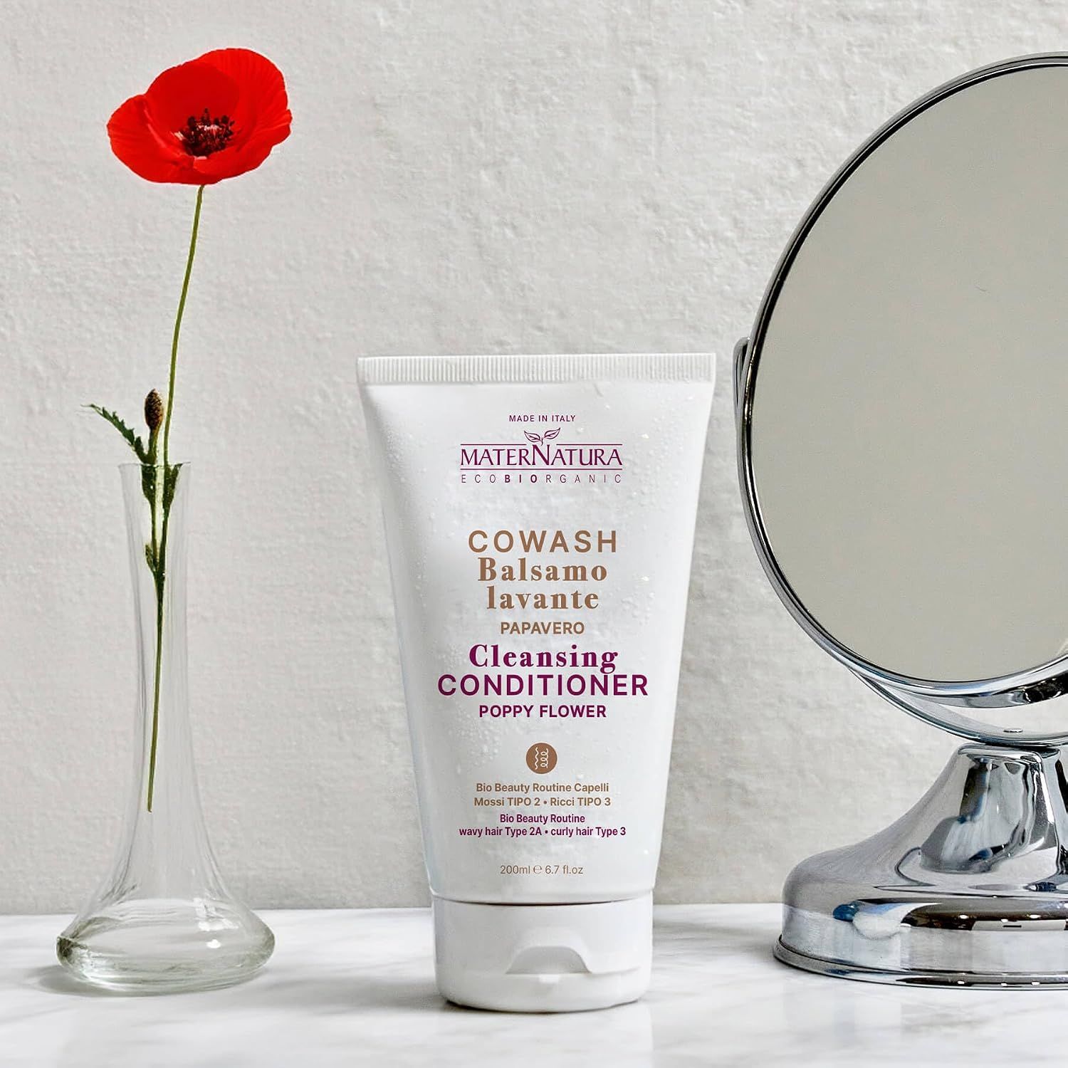 Weiße Tube mit MaterNatura Cowash Balsamo Lavante Poppy Flower. Daneben eine Vase mit Mohnblume und ein Spiegel.