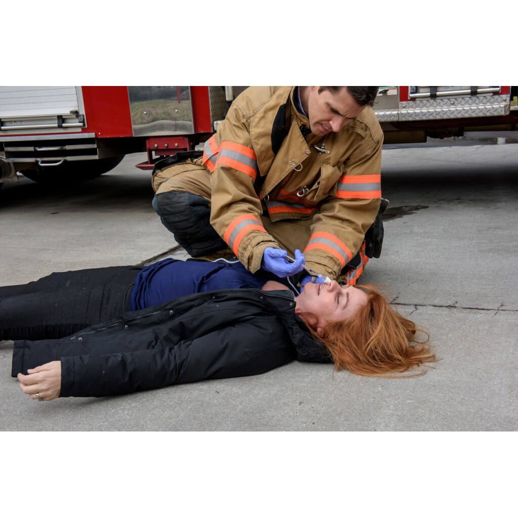 Feuerwehrmann kniet neben liegender Person und verabreicht Nasalzerstäuber-Gerät.
