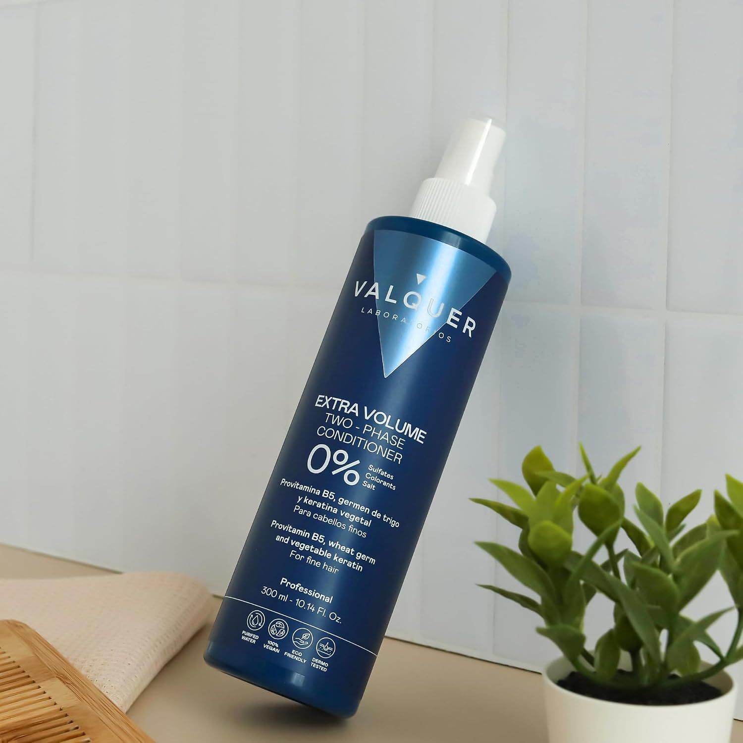 Blaue Flasche Valquer Extra Volume Two-Phase Conditioner mit Sprühkopf. Auf einem Tisch mit Pflanze.