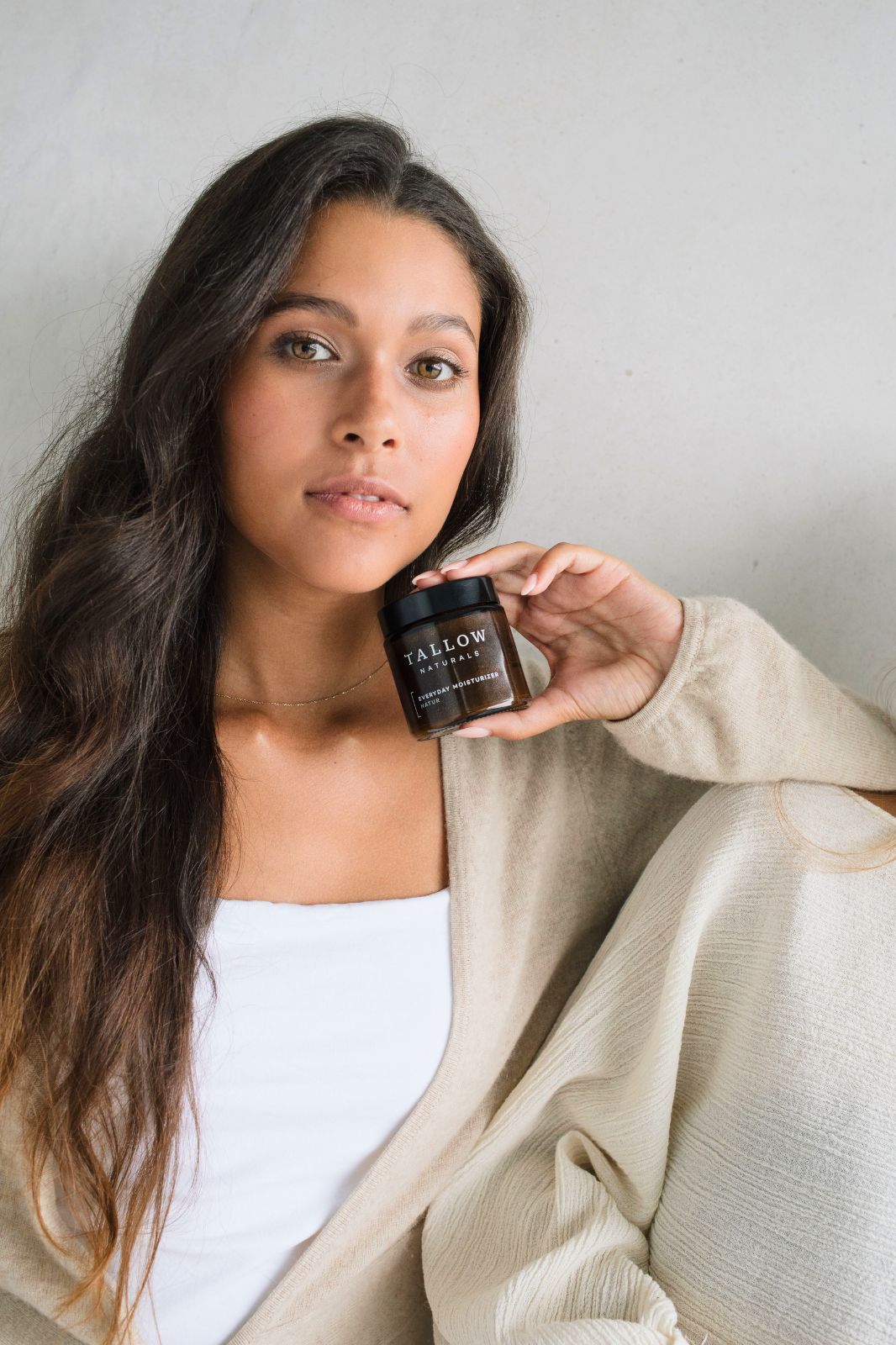 Frau hält ein braunes Glas mit schwarzem Deckel. Aufschrift: TALLOW NATURALS, BARRIER REPAIR LAVENDEL. Sie trägt einen beigen Cardigan.