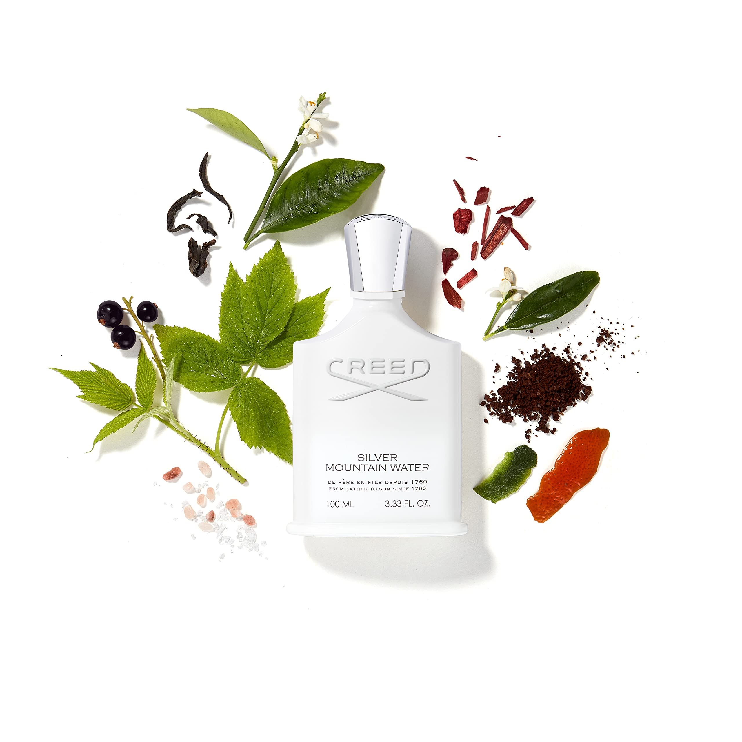 Weiße Parfumflasche umgeben von Pflanzen und Früchten. Aufschrift: Creed Silver Mountain Water.