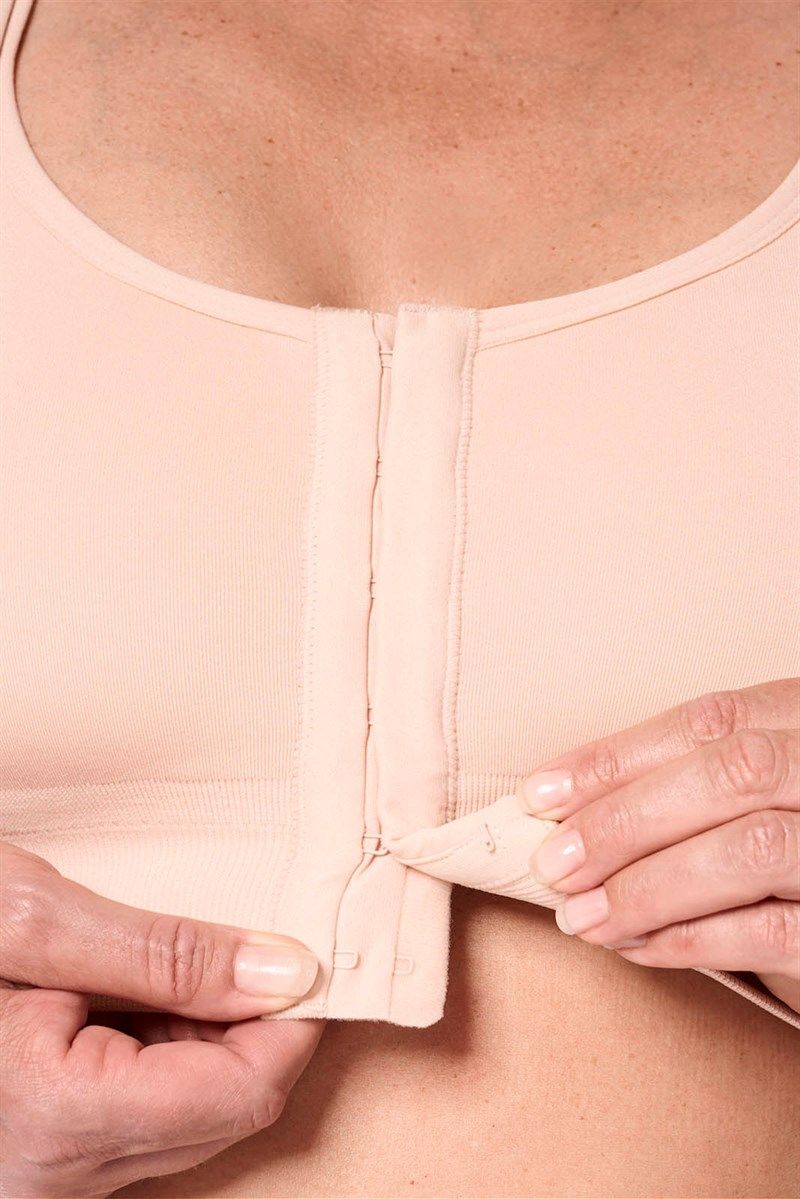 Beigefarbener BH mit Reißverschluss vorne. Hände öffnen den Verschluss.