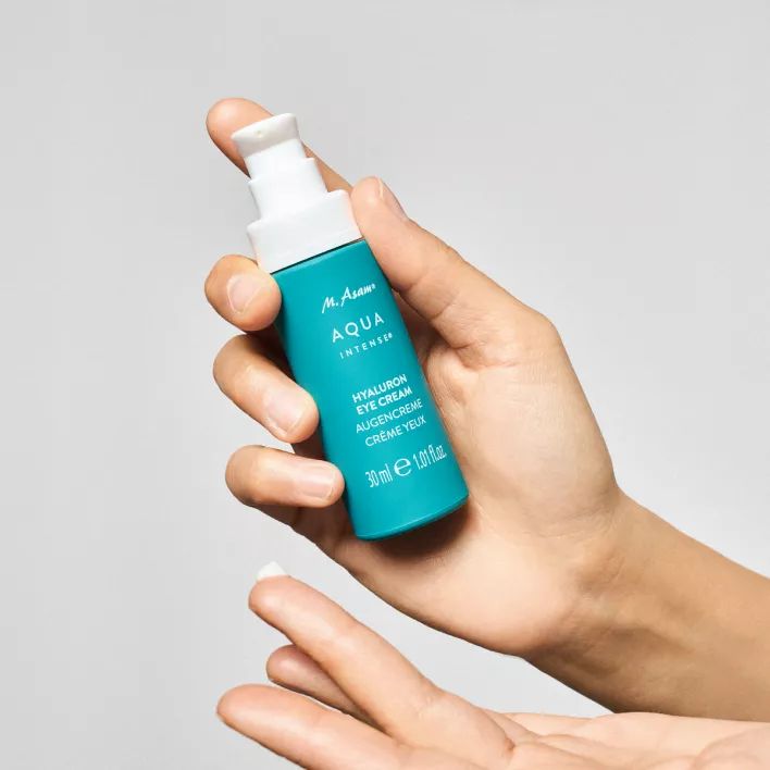 Hand hält türkisfarbene Flasche. Aufschrift: M. Asam AQUA INTENSE Hyaluron Eye Cream.