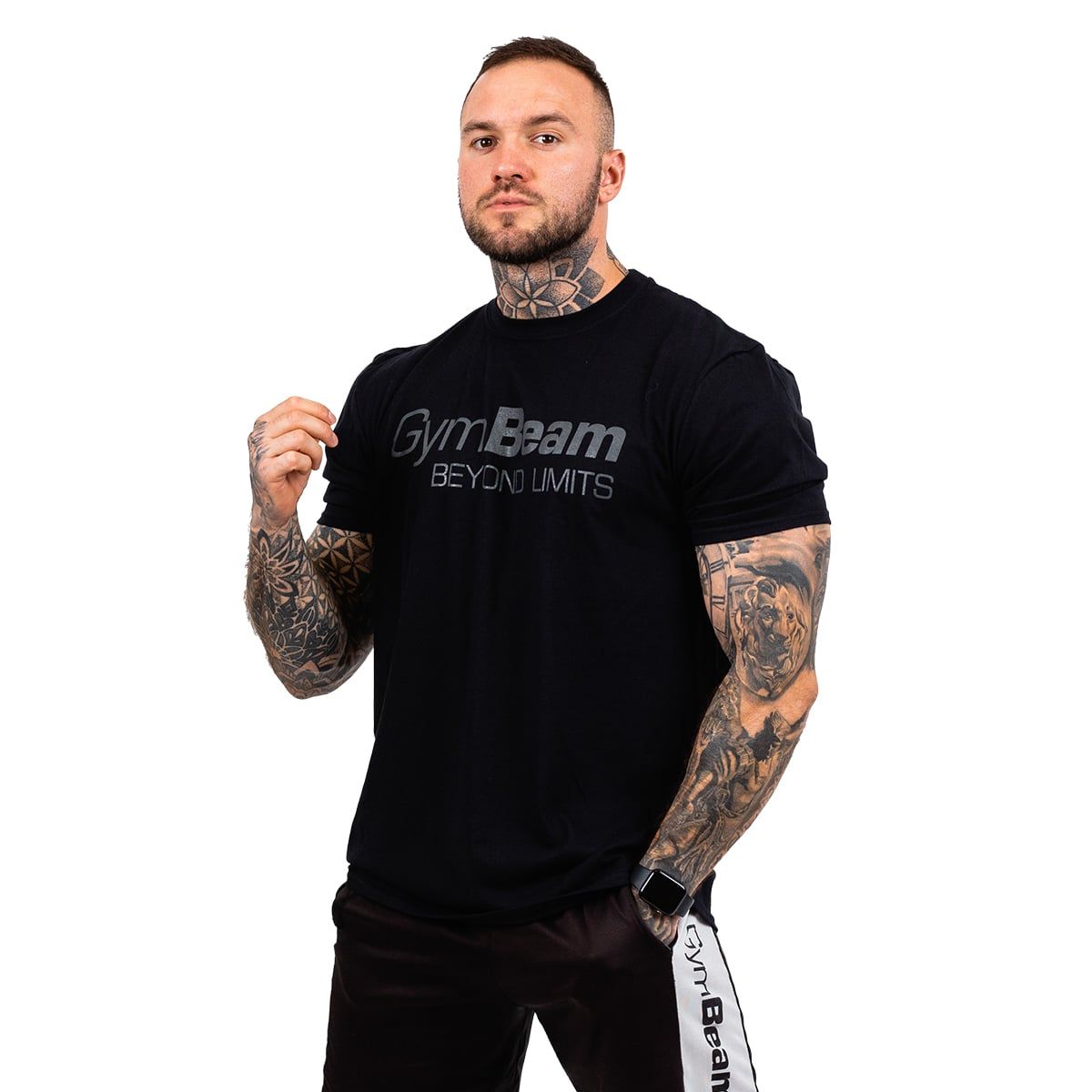Ein Mann mit Tattoos dreht sich leicht und zeigt das schwarze GymBeam T-Shirt mit "BEYOND LIMITS" Aufdruck.