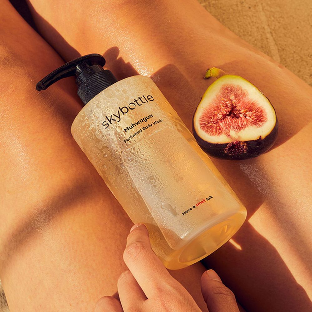 Eine Flasche SKYBOTTLE Muhwagua Duschgel liegt auf einem Bein. Daneben eine halbe Feige. Aufschrift: Muhwagua, Perfumed Body Wash. Slogan: Have a smell talk.