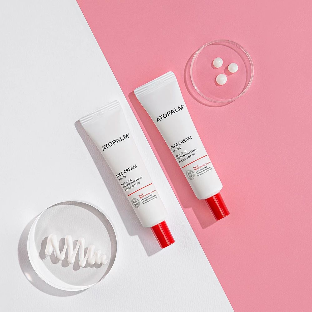 Zwei Tuben mit rotem Verschluss. Aufschrift ATOPALM FACE CREAM. Auf rosa und weißem Hintergrund.