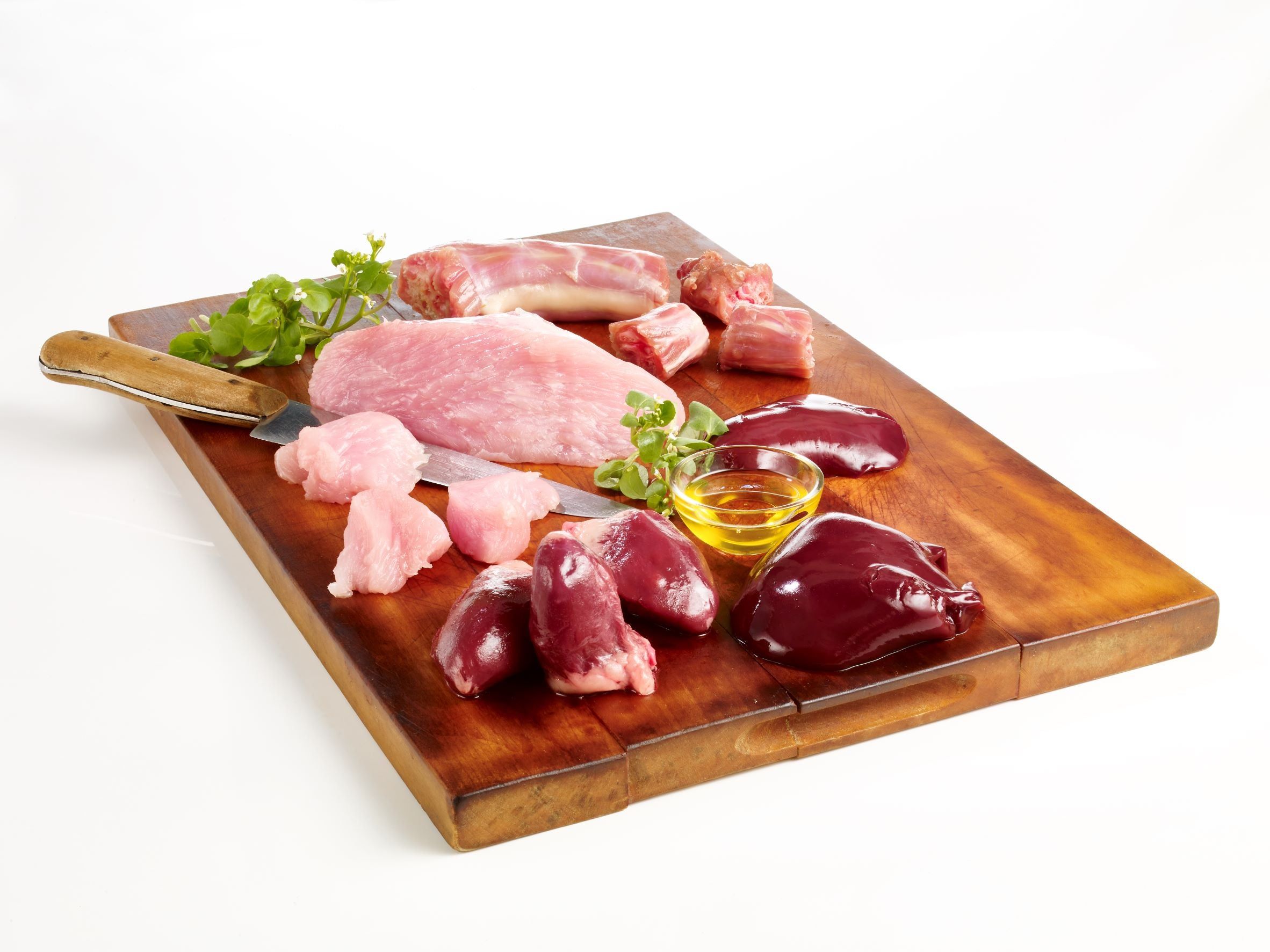 Holzbrett mit rohem Fleisch: Putenfleisch, Innereien, Kräuter und Öl. Ein Messer liegt daneben. Auf weißem Hintergrund.