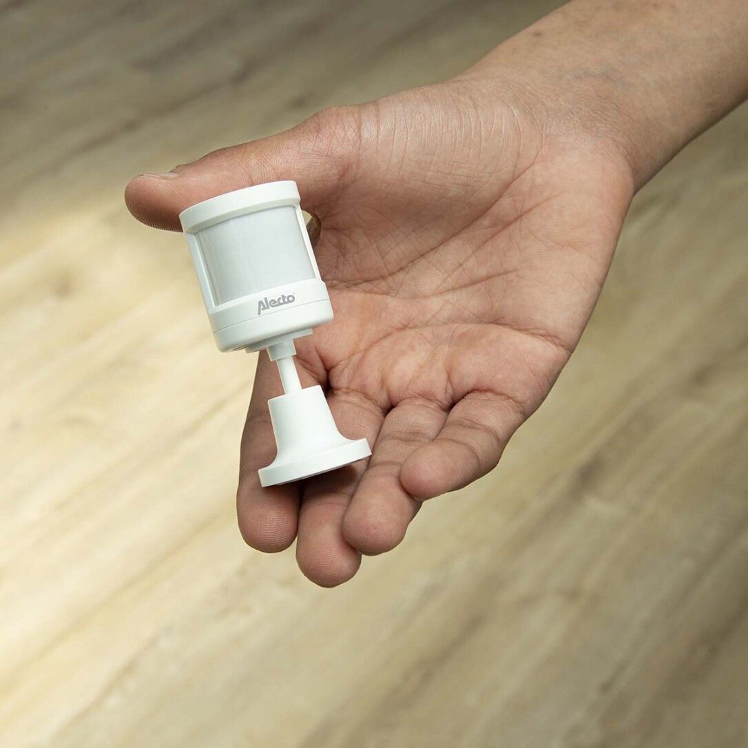 Weißer Alecto-Bewegungsmelder in einer Hand gehalten. Produktname sichtbar.
