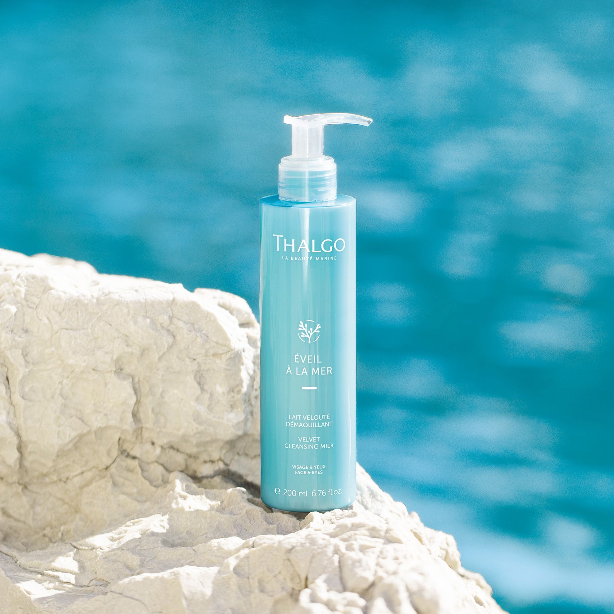 Türkisgrüne Flasche mit Pumpe auf einem Felsen vor blauem Wasser. Aufschrift: THALGO, ÉVEIL À LA MER, LAIT VELOUTÉ DÉMAQUILLANT, VELVET CLEANSING MILK.