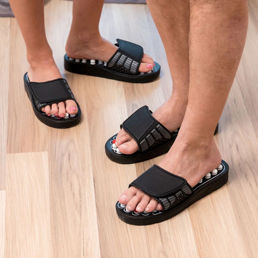 Drei Personen tragen Akupunktur-Schuhe. Schwarze Schuhe mit weißen und roten Noppen. Verstellbarer Riemen.