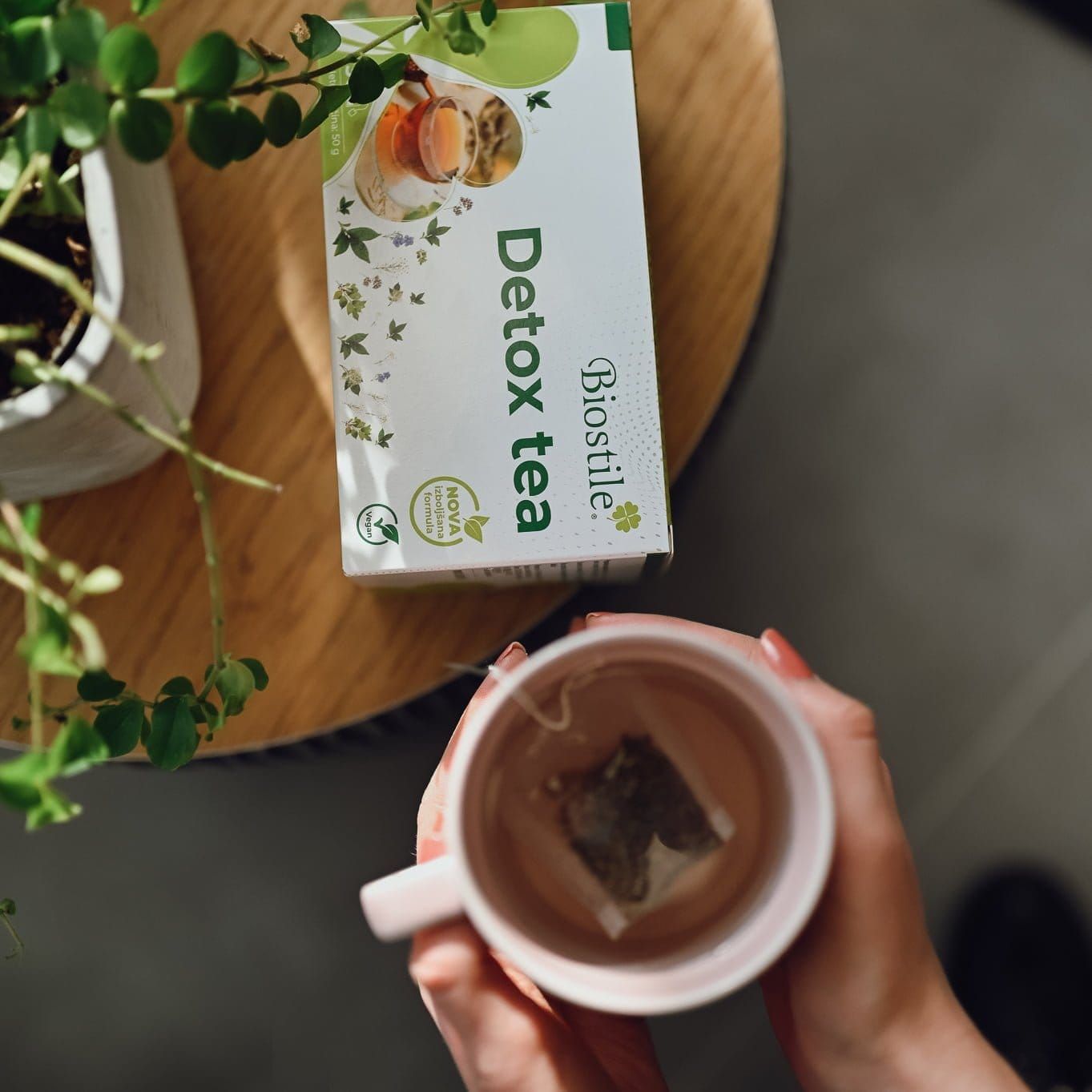 Eine Person hält eine Tasse Tee mit einem Teebeutel. Daneben eine Packung Biostile Detox Tea.