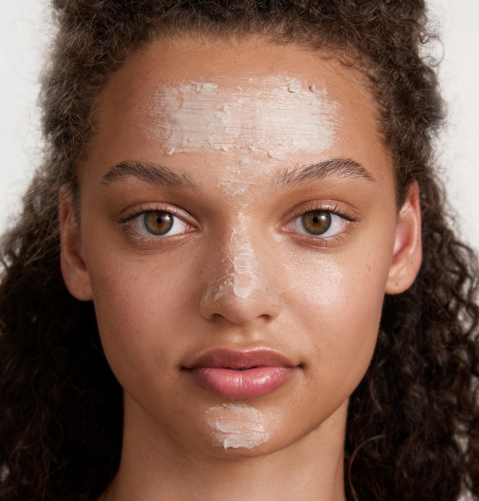 Gesicht einer Person mit Rosental Avo Clay Mask auf Stirn, Nase und Kinn. Helle Haut, braune Augen, lockiges Haar.