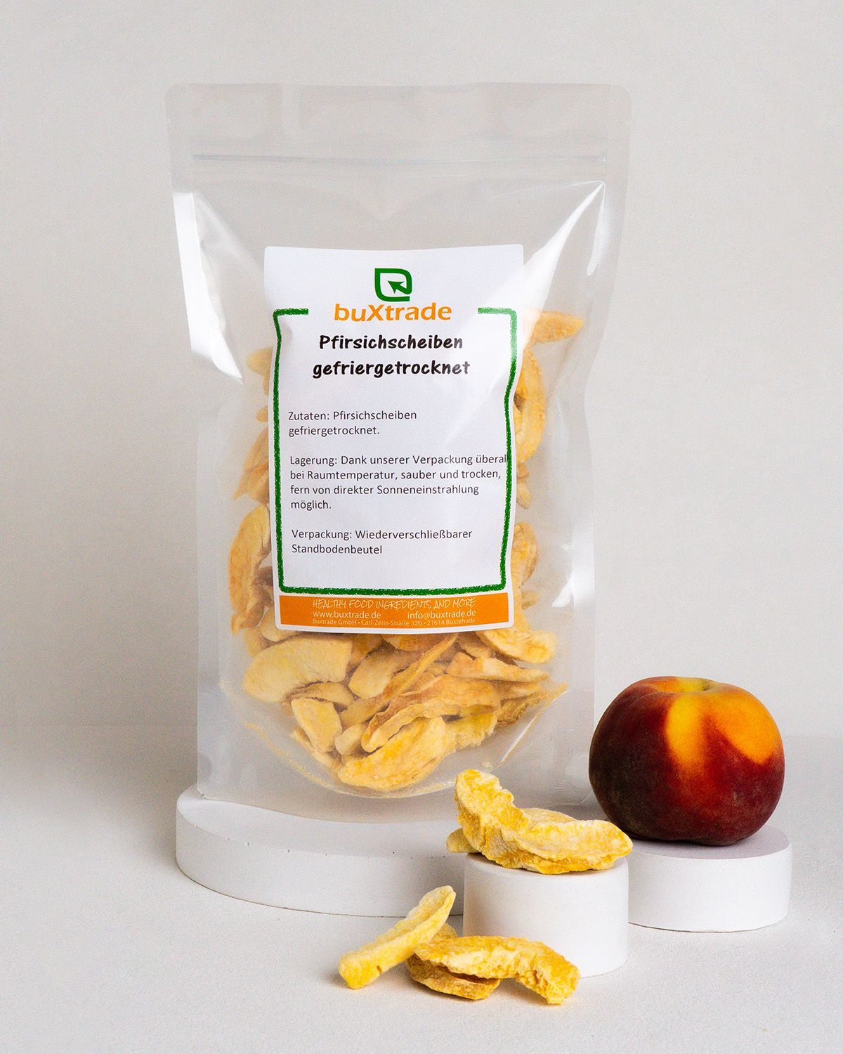 Transparente Verpackung mit getrockneten Pfirsichscheiben und frischer Pfirsich. Aufkleber: buXtrade, gefriergetrocknet.