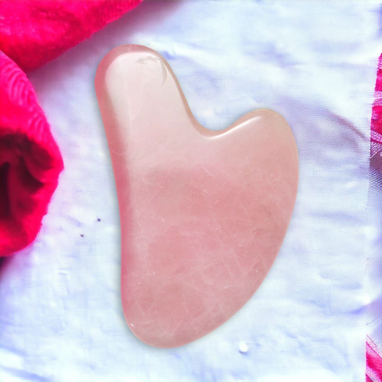 Rosa Gua Sha aus Stein, herzförmig. Auf weißem Stoff, neben einem roten Handtuch.