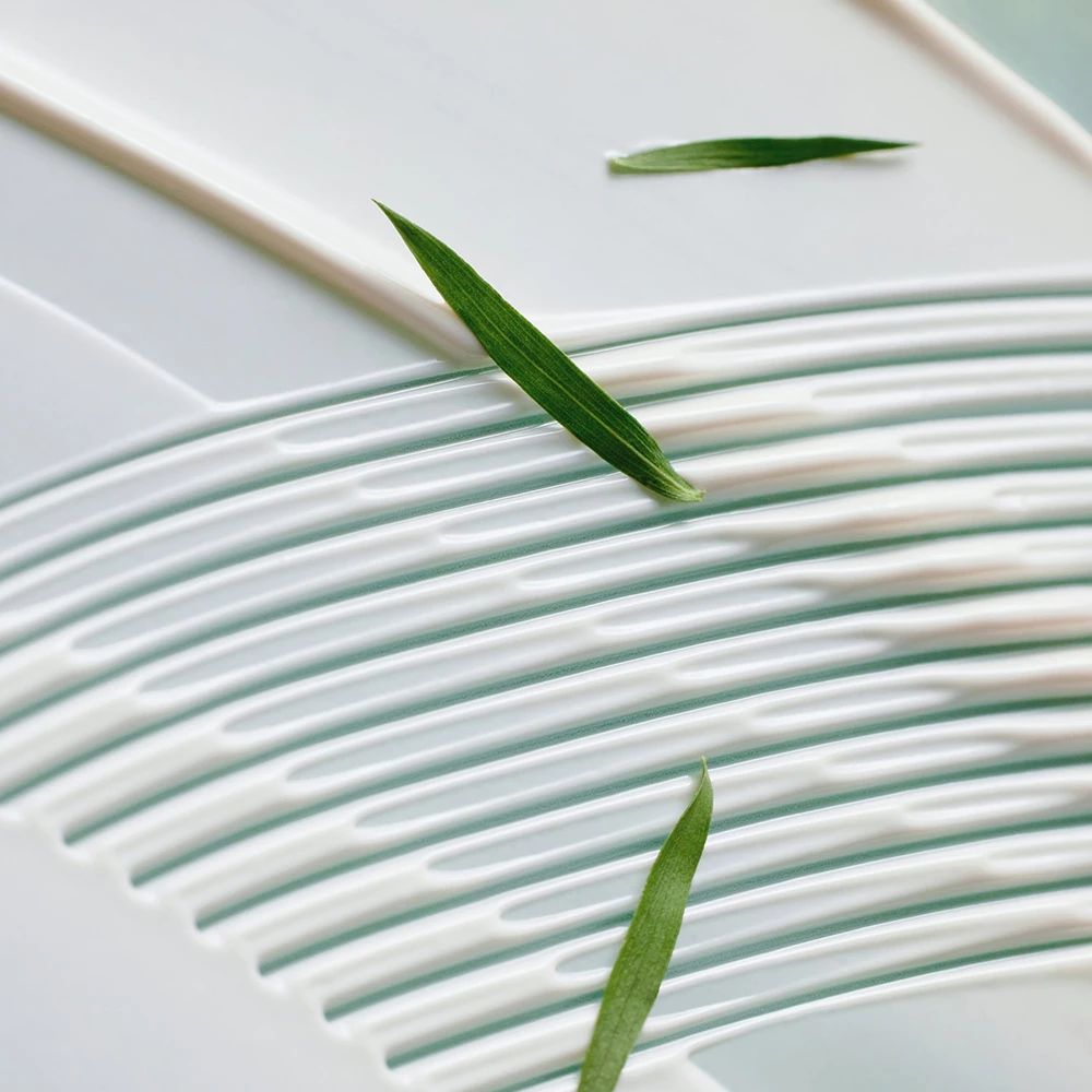 Weißer Creme-Untergrund mit grünen Blättern. Creme in Wellenform aufgetragen. Blätter liegen auf der Creme.