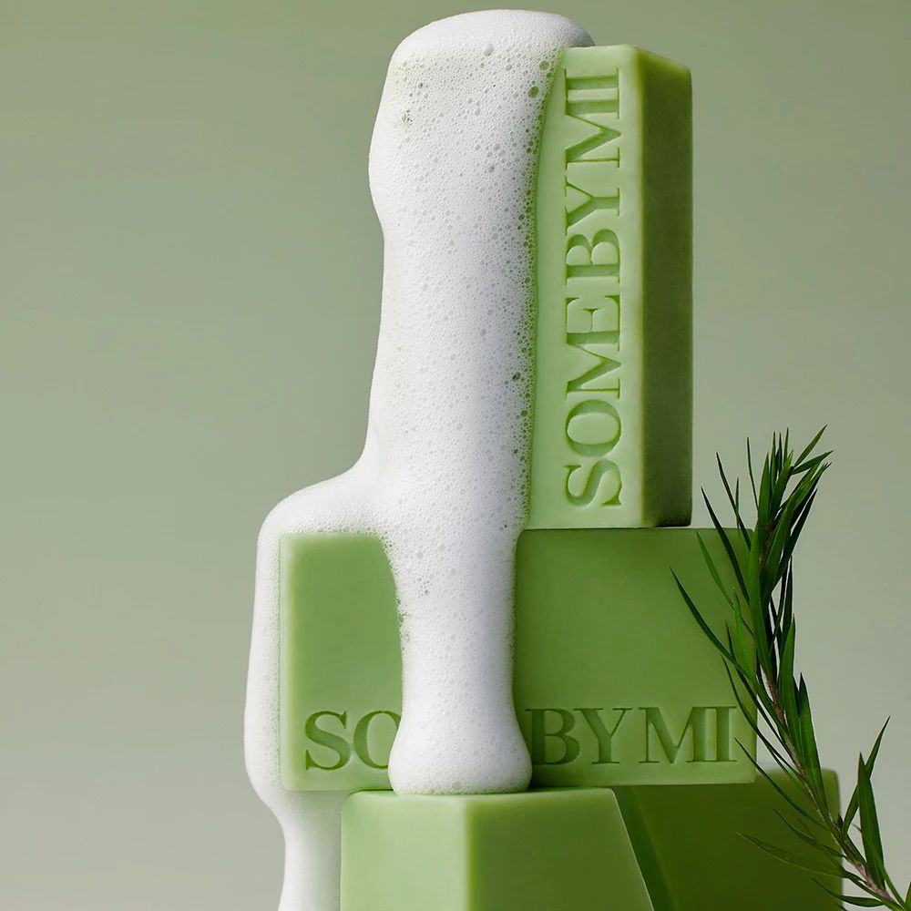 Gestapelte grüne Seifenstücke mit "SOME BY MI"-Schriftzug und Schaum.