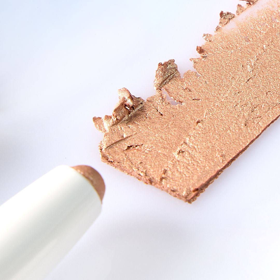 Ein weißer Stift-Lidschatten und ein Swatch. Aufschrift: "Eyeshadow 308 Sunset". Die Spitze ist in einem hellen Farbton gehalten.